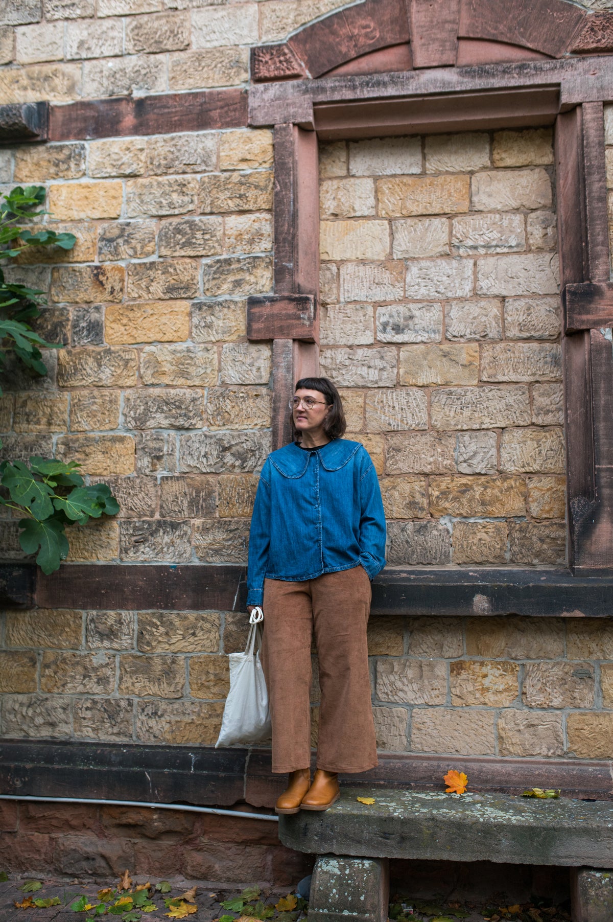 Cord-Culotte in Cognac im Ganzkörperlook mit blauem Pulli und Tasche vor Backsteinmauer