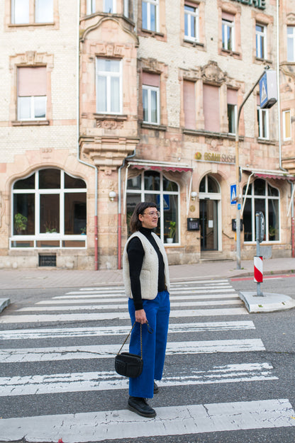 Frau in kobaltblauer Cord-Culotte mit weißer Fleeceweste und schwarzem Oberteil auf einem Zebrastreifen