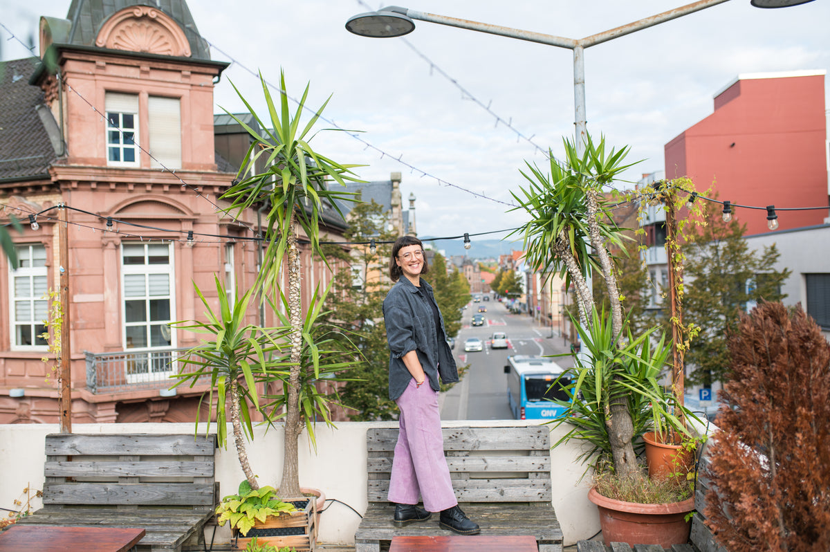 Frau in mauvefarbener Cord-Culotte auf einer Terrasse zwischen Pflanzen