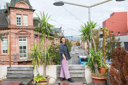 Frau in mauvefarbener Cord-Culotte auf einer Terrasse zwischen Pflanzen