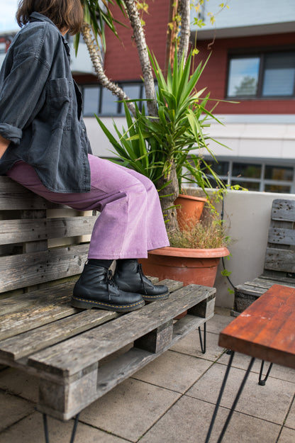 Sitzende Frau in mauvefarbener Cord-Culotte, dunkler Jacke und schwarzen Stiefeln