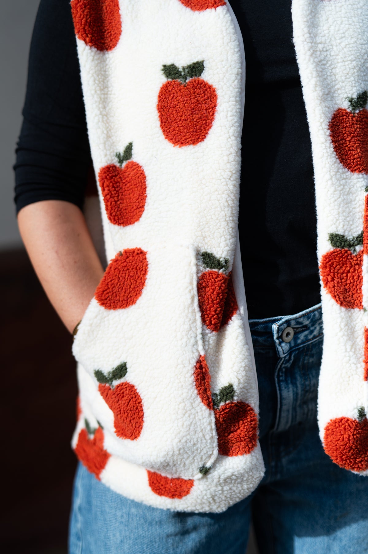 Nahaufnahme der Teddyweste Apple Hug mit roten Äpfeln und aufgesetzter Tasche"