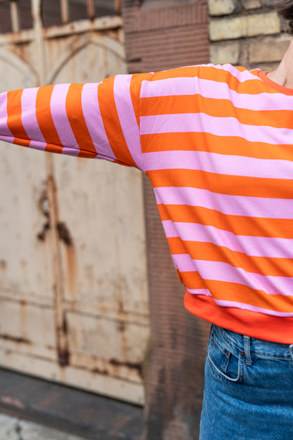 Orange-rosa gestreifter Oversize-Sweatpullover, weiter Ärmel in Nahaufnahme vor rostigem Tor