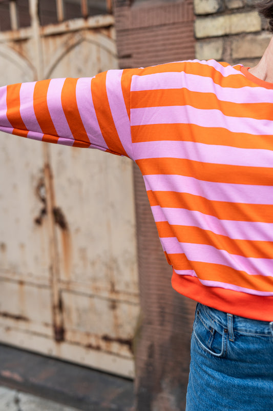 Orange-rosa gestreifter Oversize-Sweatpullover, weiter Ärmel in Nahaufnahme vor rostigem Tor