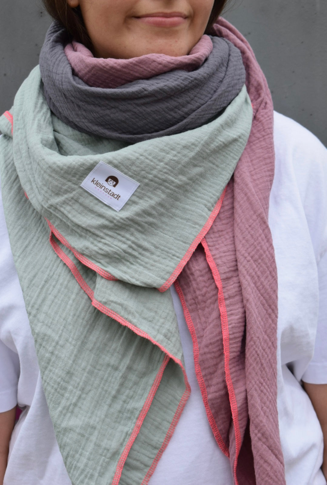Musselinschal Salbei, Grau, Mauve um den Hals geschlungen, Crinkle-Struktur und Neonpink-Naht im Detail