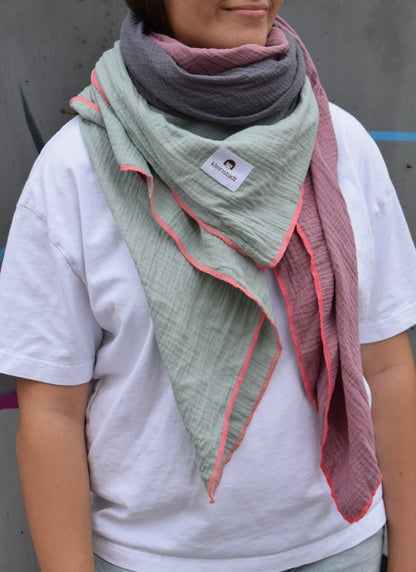 Frau trägt Musselinschal in Salbei, Grau und Mauve mit Neonpink-Kontrastnaht, locker über weißem Shirt drapiert